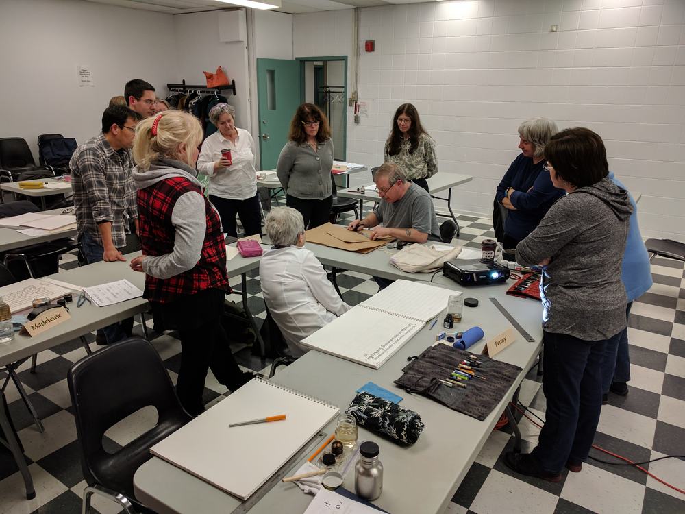Students observe instructor Rick Draffin ruling up Kraft paper for a writing demonstration