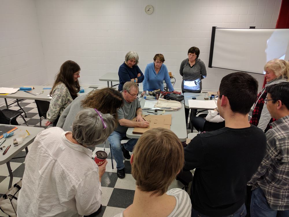 Students observe as instructor Rick Draffin writes large Foundational letters on Kraft paper using an automatic pen